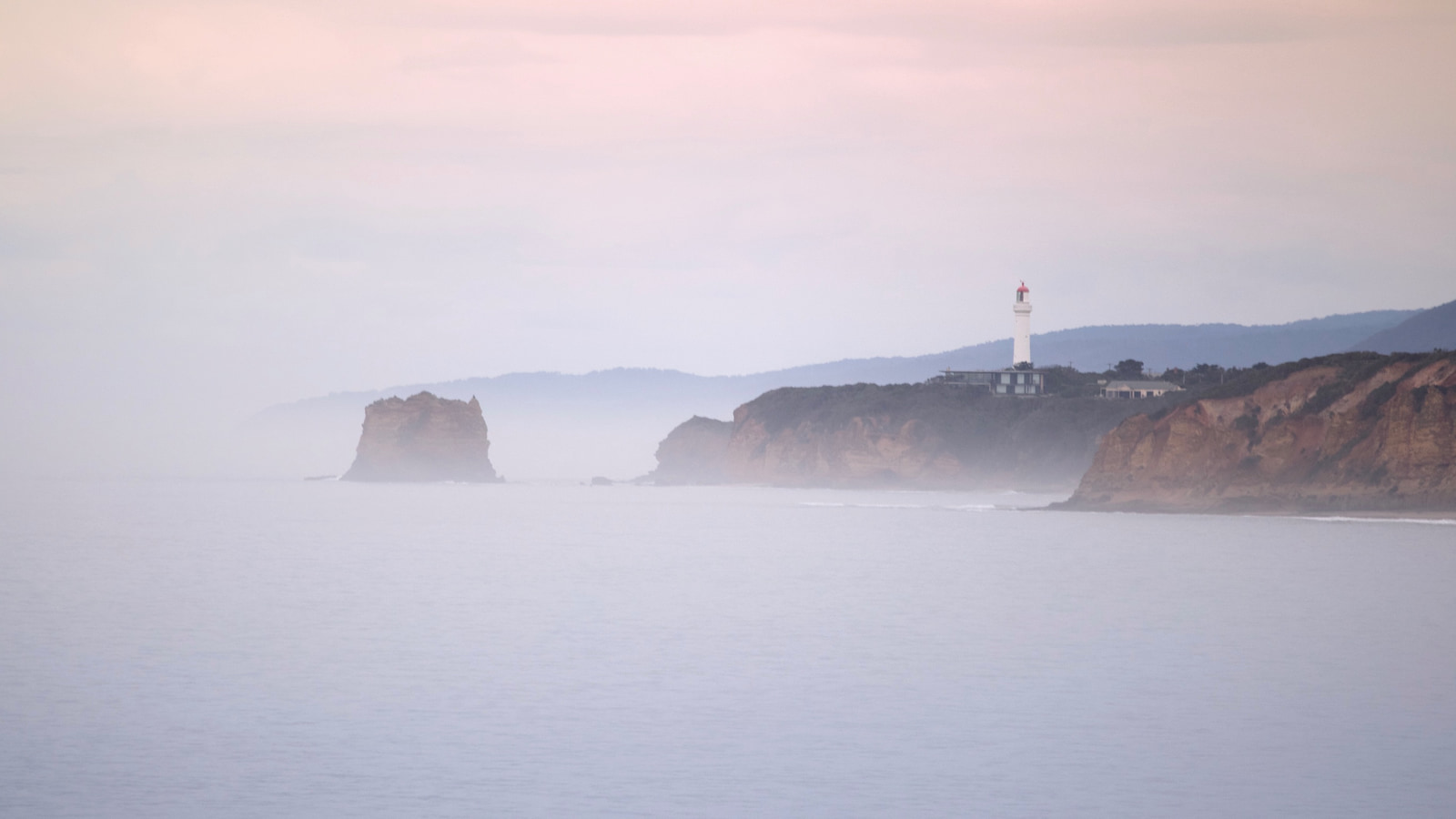 A lighthouse stands on a cliff overlooking a misty ocean.